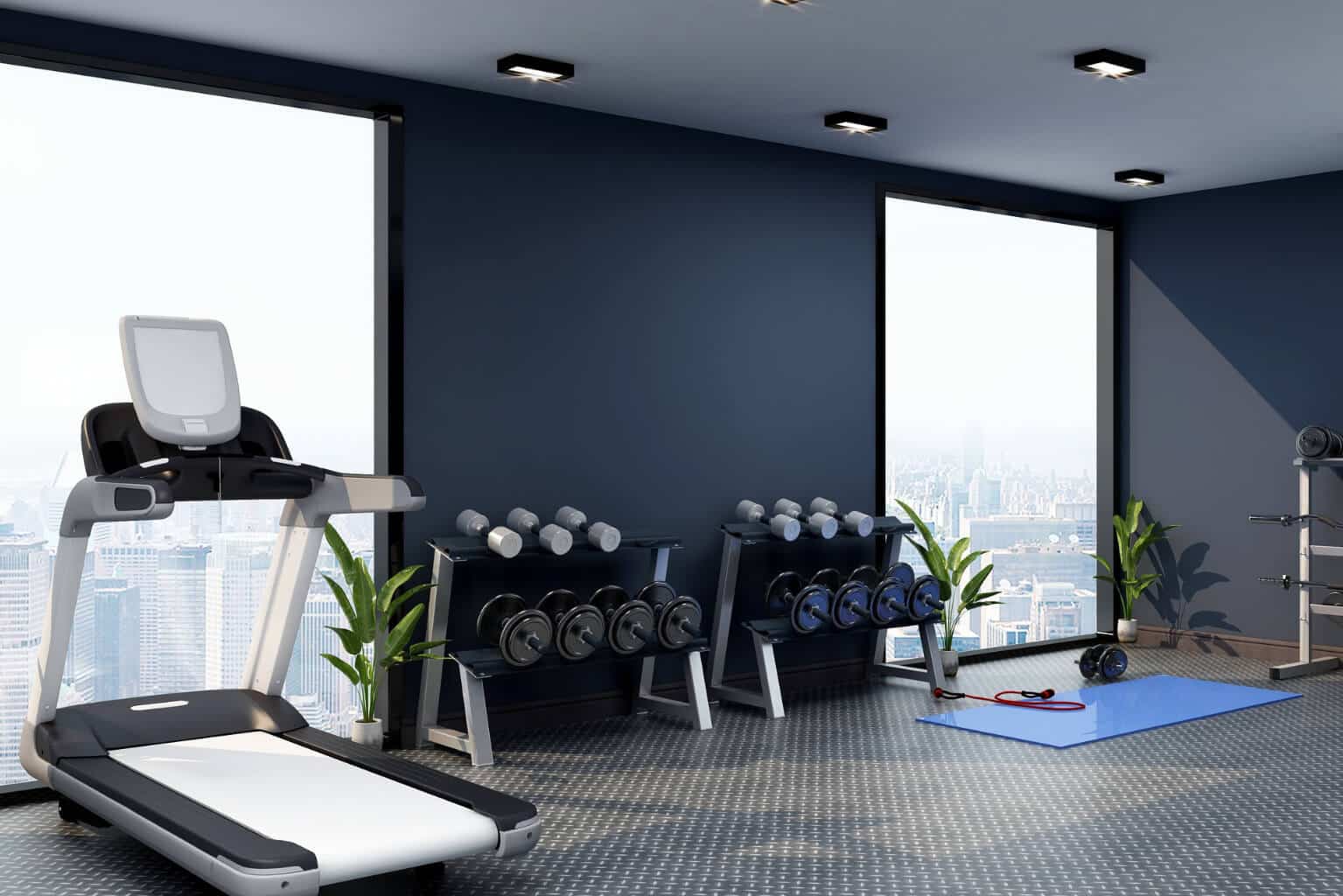 Sleek fitness studio featuring a dark navy wall, treadmill, dumbbell racks, blue yoga mat, and large windows with a city skyline view.